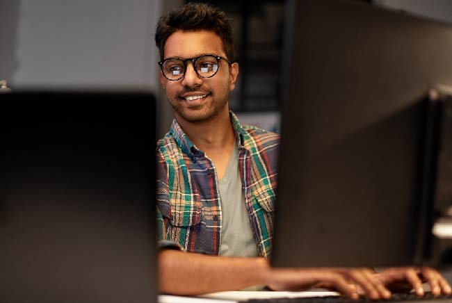 A male employee sat working in between 2 desktop computers